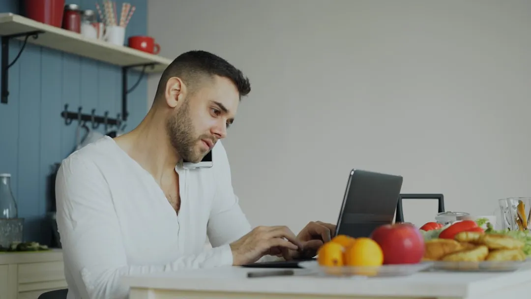 Man using phone and laptop at kitchen table